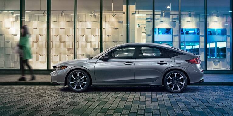 2027 Honda Civic Hatchback Sport Touring Hybrid in Solar Silver Metallic profile parked at night (Compact Hatchback).